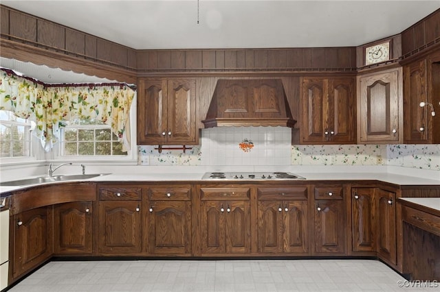 kitchen with sink, dark brown cabinets, stovetop, and custom range hood