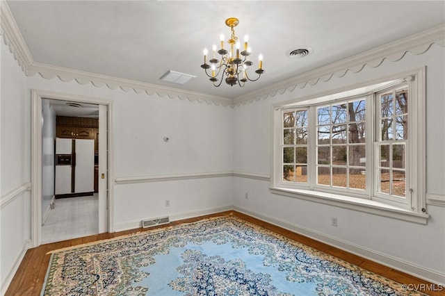 spare room featuring a wealth of natural light, wood-type flooring, crown molding, and an inviting chandelier