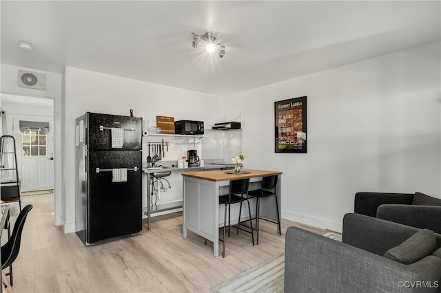 kitchen featuring black appliances, a breakfast bar, butcher block countertops, and light hardwood / wood-style floors