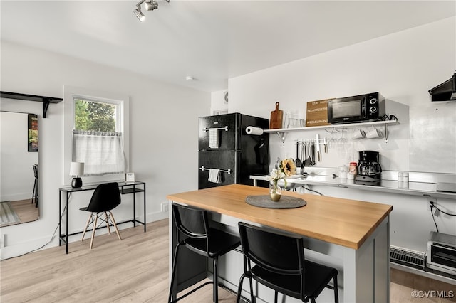 kitchen with black appliances, butcher block countertops, a kitchen bar, and light hardwood / wood-style floors