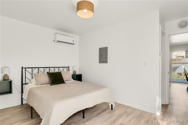 bedroom featuring electric panel, light wood-type flooring, and a wall mounted air conditioner