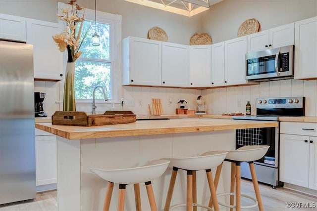 kitchen with wood counters, appliances with stainless steel finishes, a kitchen bar, and white cabinets