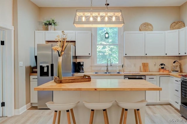 kitchen featuring a breakfast bar, wood counters, white cabinets, and hanging light fixtures