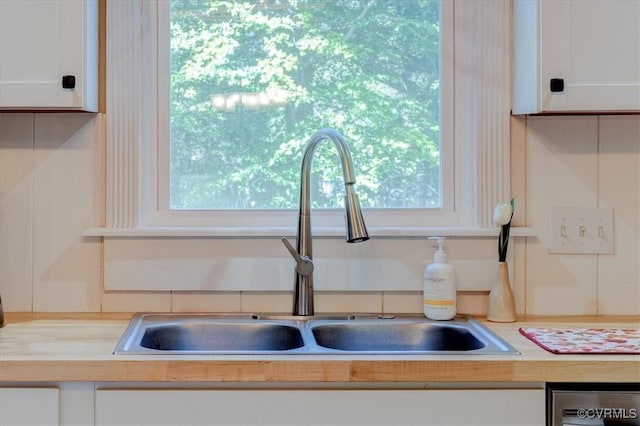 interior details with wood counters, white cabinets, dishwasher, and sink