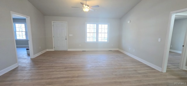 empty room with ceiling fan, a wealth of natural light, light wood-type flooring, and vaulted ceiling