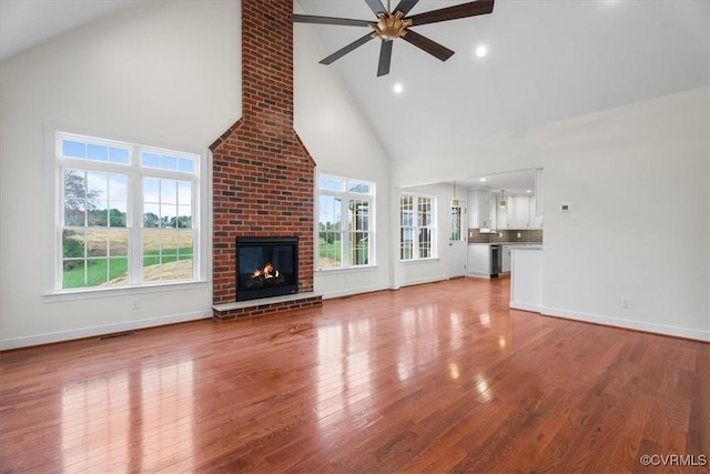 unfurnished living room featuring high vaulted ceiling, light hardwood / wood-style flooring, a brick fireplace, and ceiling fan