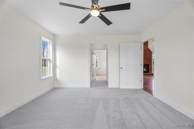 carpeted empty room featuring ceiling fan and a brick fireplace