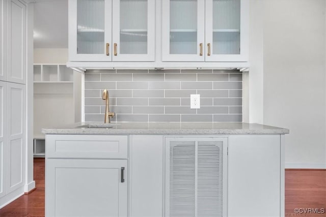 bar with tasteful backsplash, sink, white cabinetry, hardwood / wood-style flooring, and light stone countertops