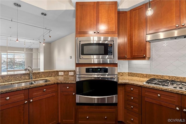 kitchen featuring light stone countertops, appliances with stainless steel finishes, rail lighting, hanging light fixtures, and sink