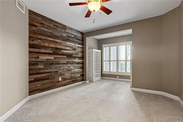 carpeted empty room featuring ceiling fan and wood walls