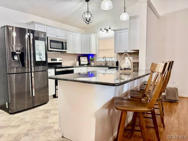 kitchen with white cabinets, appliances with stainless steel finishes, decorative light fixtures, dark stone countertops, and sink