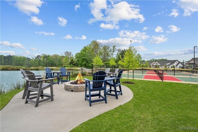 view of community with tennis court, a yard, a fire pit, and a water view