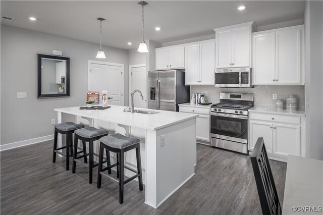 kitchen with hanging light fixtures, white cabinets, stainless steel appliances, and an island with sink