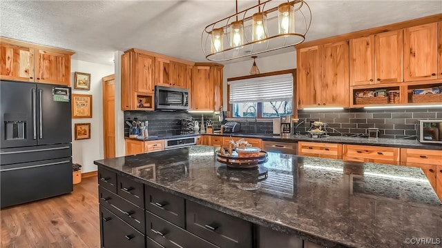 kitchen featuring decorative light fixtures, light wood-type flooring, appliances with stainless steel finishes, dark stone counters, and backsplash