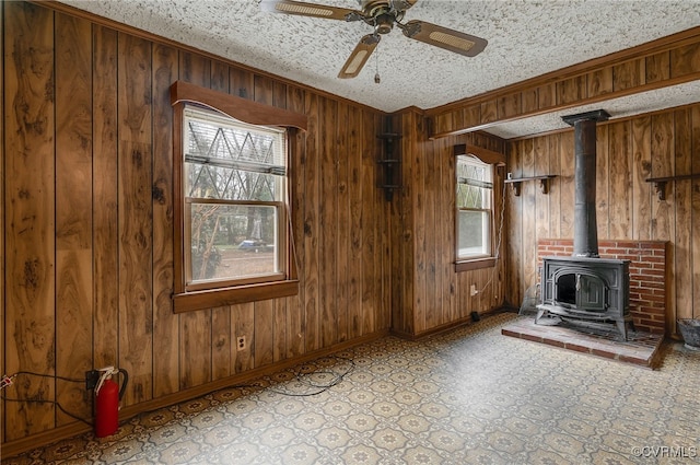 unfurnished living room featuring a wood stove, ceiling fan, ornamental molding, a textured ceiling, and wood walls