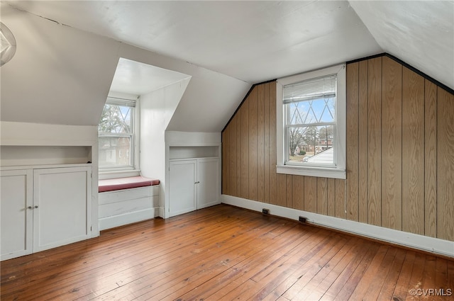 bonus room featuring vaulted ceiling, wooden walls, and light hardwood / wood-style floors