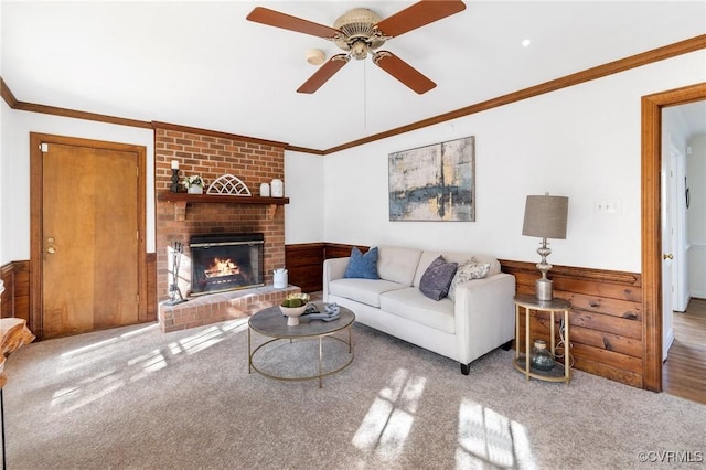 living room with crown molding, a brick fireplace, carpet flooring, wooden walls, and ceiling fan