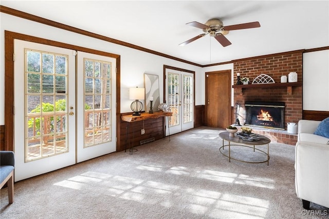 living room with french doors, a brick fireplace, ornamental molding, carpet floors, and ceiling fan