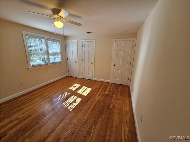 unfurnished bedroom featuring ceiling fan, hardwood / wood-style flooring, and two closets