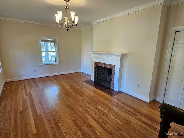 unfurnished living room featuring a brick fireplace, wood-type flooring, ornamental molding, and an inviting chandelier