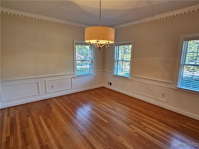 empty room with hardwood / wood-style floors, ornamental molding, and a chandelier