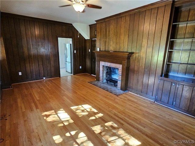 unfurnished living room with ceiling fan, a fireplace, wood walls, light hardwood / wood-style flooring, and built in features