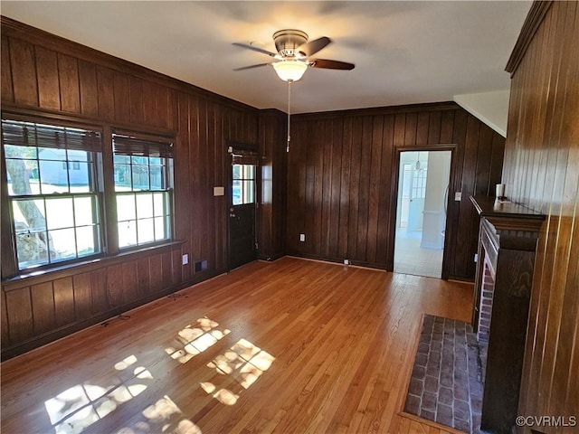 interior space with ceiling fan, light hardwood / wood-style floors, and wooden walls