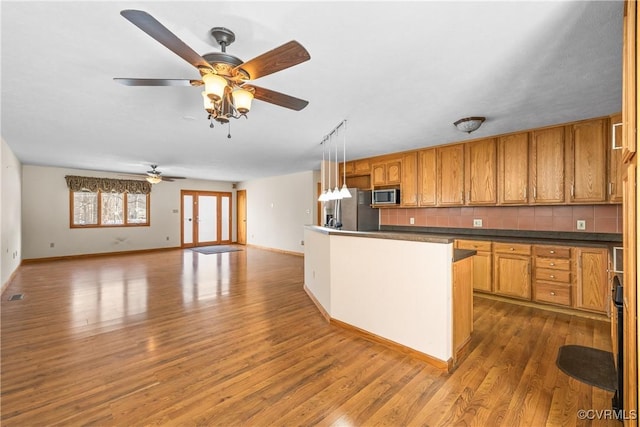 kitchen with dark hardwood / wood-style flooring, pendant lighting, ceiling fan, stainless steel appliances, and backsplash