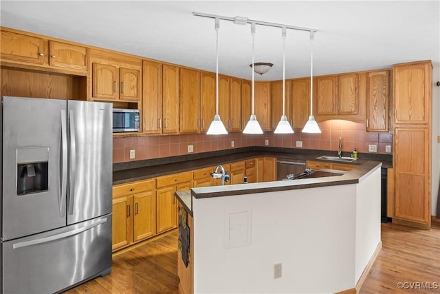 kitchen with appliances with stainless steel finishes, decorative light fixtures, tasteful backsplash, wood-type flooring, and sink