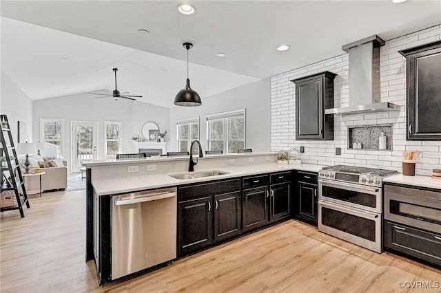 kitchen with wall chimney range hood, stainless steel appliances, decorative backsplash, sink, and vaulted ceiling