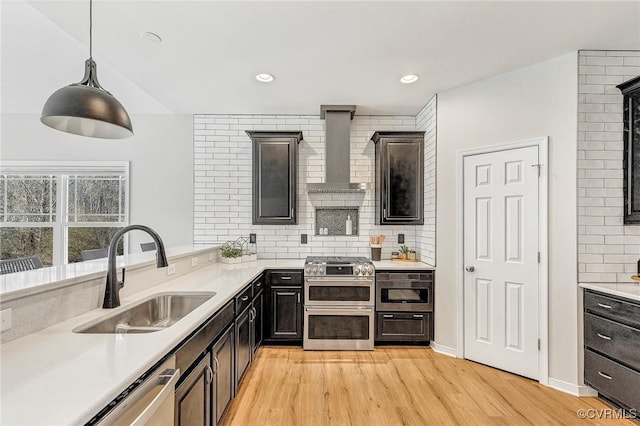 kitchen with decorative backsplash, sink, wall chimney range hood, pendant lighting, and stainless steel appliances