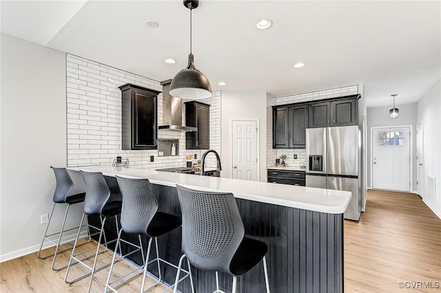 kitchen featuring a kitchen bar, stainless steel fridge with ice dispenser, hanging light fixtures, decorative backsplash, and kitchen peninsula