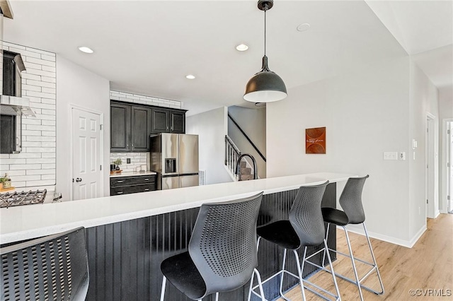 kitchen featuring decorative light fixtures, backsplash, stainless steel fridge with ice dispenser, kitchen peninsula, and a breakfast bar area