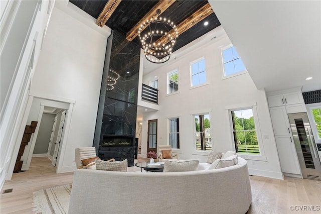 living area featuring a notable chandelier, a towering ceiling, light wood-type flooring, and baseboards