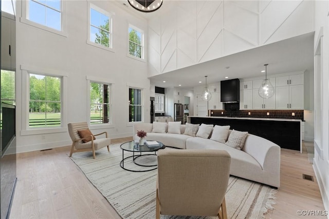 living area with light wood finished floors, visible vents, a high ceiling, and baseboards