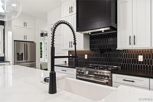 kitchen with appliances with stainless steel finishes, backsplash, wall chimney range hood, and white cabinetry