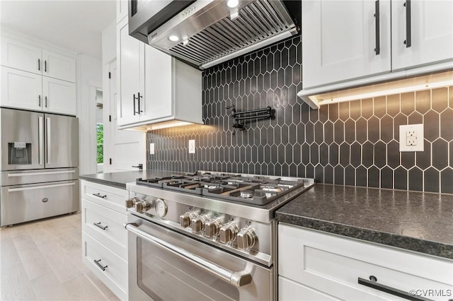 kitchen featuring white cabinets, dark stone counters, custom exhaust hood, stainless steel appliances, and backsplash