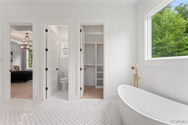 full bathroom with toilet, a soaking tub, and a notable chandelier