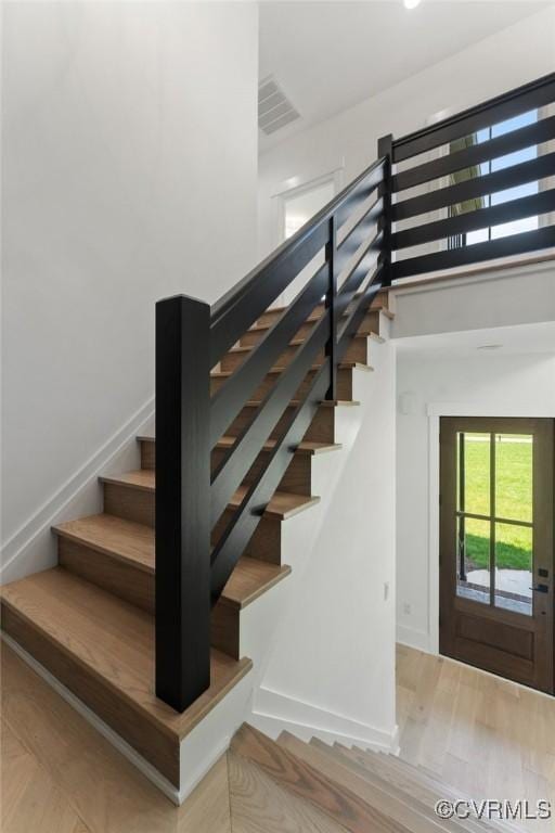 stairs with a high ceiling, visible vents, baseboards, and wood finished floors