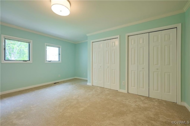 unfurnished bedroom featuring light carpet, two closets, and ornamental molding