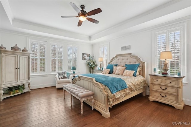 bedroom featuring dark wood-type flooring, ceiling fan, ornamental molding, and a raised ceiling