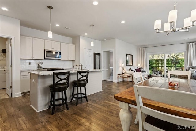 kitchen with pendant lighting, white cabinetry, dark hardwood / wood-style flooring, tasteful backsplash, and a center island with sink