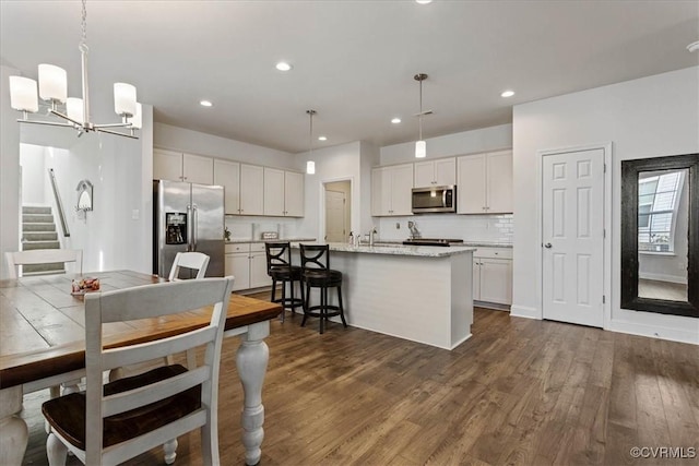 kitchen with a center island with sink, stainless steel appliances, backsplash, decorative light fixtures, and white cabinets