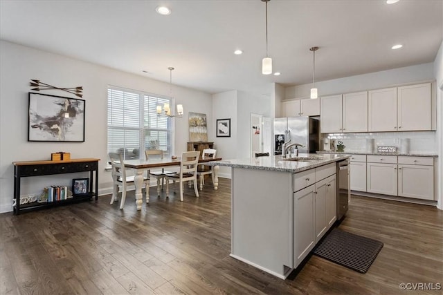 kitchen featuring an island with sink, appliances with stainless steel finishes, dark hardwood / wood-style flooring, hanging light fixtures, and light stone countertops