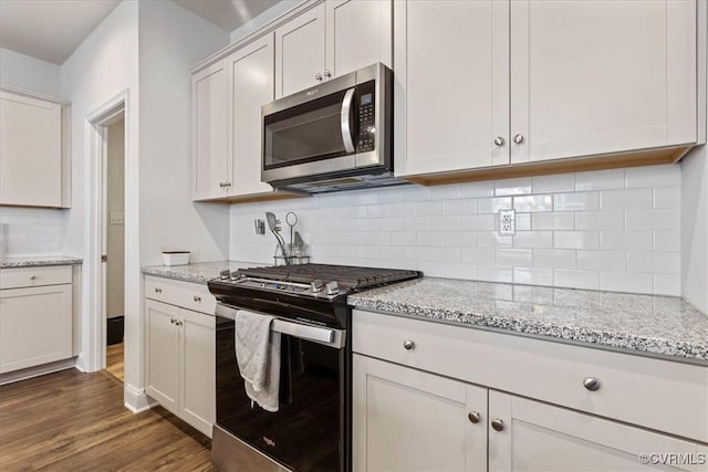 kitchen with light stone countertops, white cabinetry, appliances with stainless steel finishes, and dark hardwood / wood-style floors