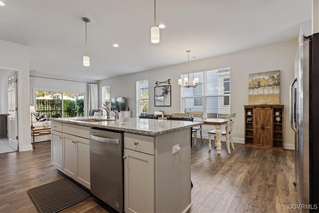 kitchen featuring decorative light fixtures, sink, white cabinetry, appliances with stainless steel finishes, and an island with sink