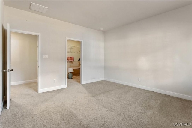 unfurnished bedroom with a walk in closet, a closet, and light colored carpet