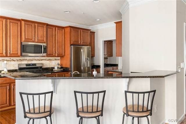 kitchen featuring kitchen peninsula, stainless steel appliances, a breakfast bar area, and dark stone countertops