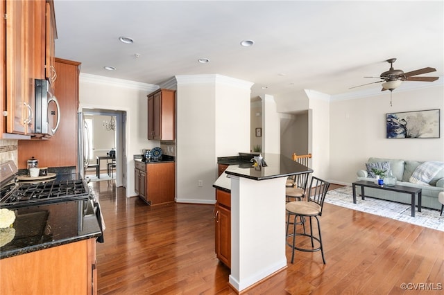 kitchen with crown molding, appliances with stainless steel finishes, dark hardwood / wood-style flooring, ceiling fan, and a breakfast bar area