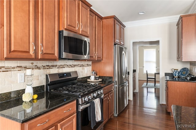 kitchen with appliances with stainless steel finishes, tasteful backsplash, ornamental molding, dark wood-type flooring, and dark stone counters